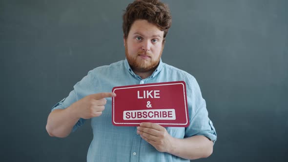 Young Male Vlogger Showing Like and Subscribe Sign and Thumbsup Hand Gesture on Gray Background alt