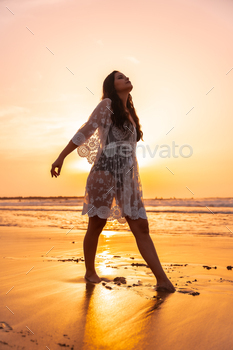 Silhouette of a woman on a beach at sunset in a white dress enjoying the summer