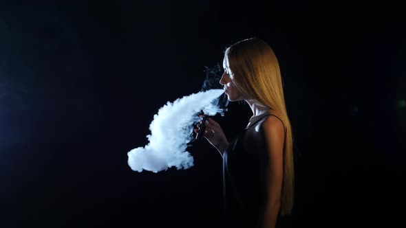 Blonde in a Spacious Room Smokes an Electronic Cigarette, Black Background alt