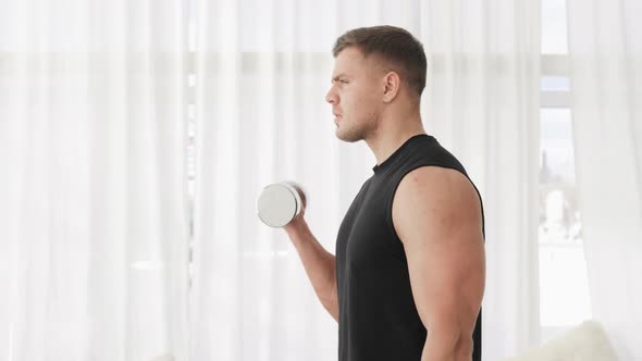 Young Man Bodybuilder Is Lifting Dumbbells at Home Practicing Biceps Exercise