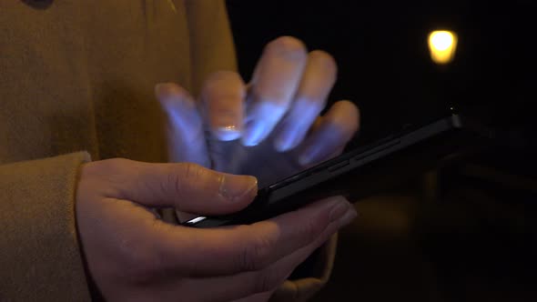 A Woman Works on a Smartphone in an Urban Area at Night, Streetlight in the Background alt