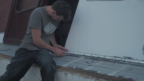 Young caucasian carpenter trimming excess sikaflex sealant on wooden boat trim alt