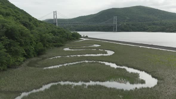 Drone shot of a little winding creek,ing forwards and panning up, revealing a bridge in the backgrou alt