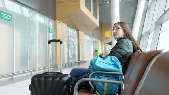 Young Tired Woman is Waiting Her Flight in Airport Sitting in Hall alt