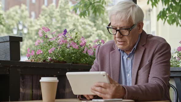 Senior Businessman Working on Tablet Over Coffee in Outdoor Restaurant alt