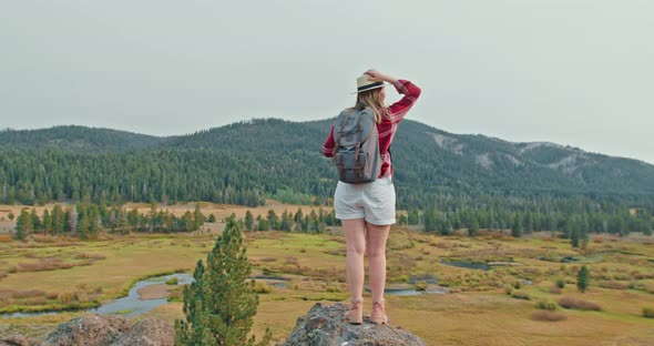 Traveler with Backpack in Red Classic Shirt Standing on Top of Rock on Fall Day alt