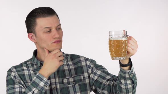 Young Man Rubbing His Chin Thoughtfully, Examining Beer in a Mug alt