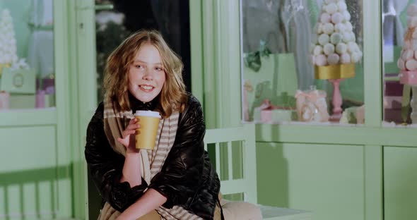 Smiling Young Girl with Paper Cup Sitting in Candy Shop alt