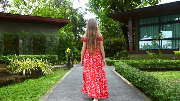 Traveller Woman in Red Dress Walking Barefoot on Path in Modern Tropical Resort alt