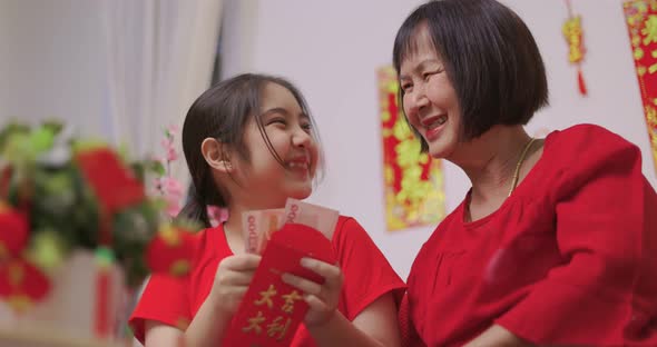 Happy Senior Asian Woman Giving Her Granddaughter A Lucky Red Envelope for Chinese New Year Gift. alt