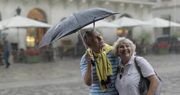 Happy Senior Tourists Stand Downtown and Enjoy the Rainy Weather in Lviv alt