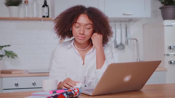 Young African American Woman Inserts Wireless Headphones Sits at Kitchen Table alt