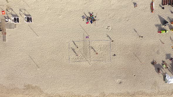 AERIAL: High Altitude Locked Shot of People Playing Volleyabll and Long Shadows on Beach