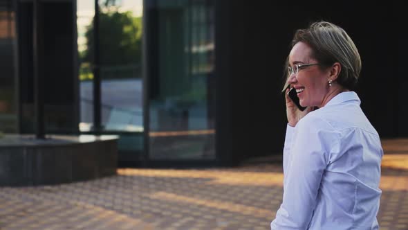 Smiling Female Professional Talking on Smart Phone Outside Office Building alt