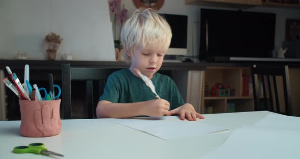 Cute Child Boy Sitting at the Table and Drawing Using Quill Pen in Living Room alt