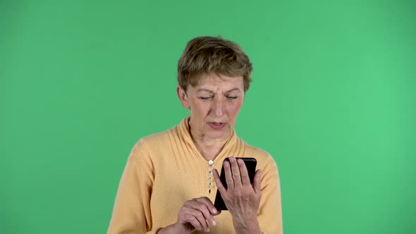 Portrait of Elderly Woman Is Talking for Video Chat Using Mobile Phone Isolated Over Green alt