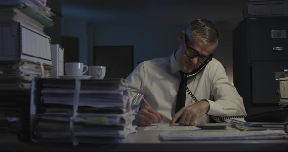 Frustrated businessman sitting at desk and working overtime, he answers a phone call and gets angry