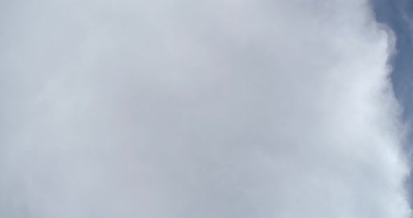 Time-lapse of clouds straight overhead as they fly by. A large cloud covers most of the shot and the alt