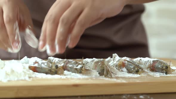 Hands of chef sprinkling and coating shrimps with flour preparing for cooking