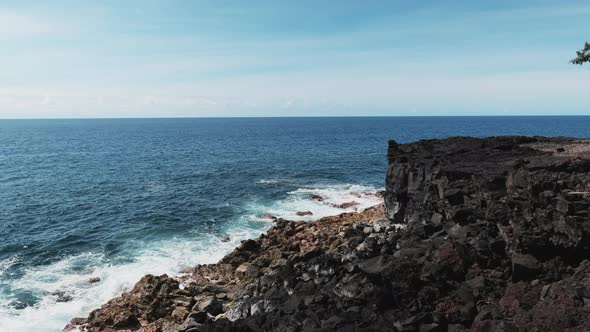 Blue waves of Pacific Ocean break against basalt cliff, Hawaii. alt