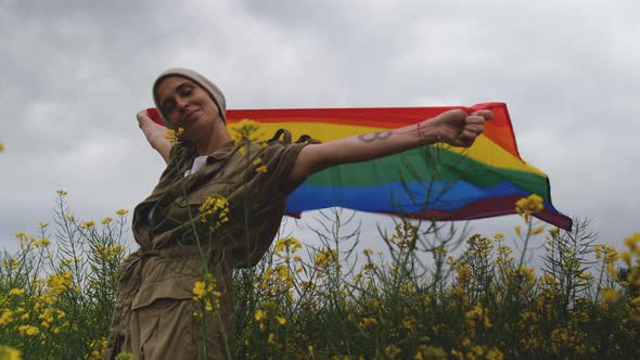 Middle aged woman with LGBT flag on field with yellow flowers alt