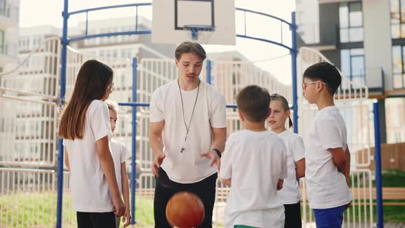 Basketball Coach Shows School Kids How to Throw the Ball Into the Basket on Basket Court alt