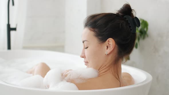 Pretty Girl Enjoying Warm Relaxing Bath Touching Gentle White Foam in Bathroom alt