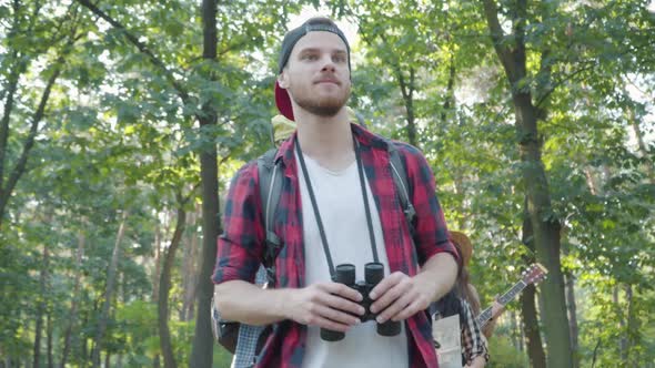 Confident Male Guide in Summer Forest with Group of Positive Young Tourists Strolling at the alt