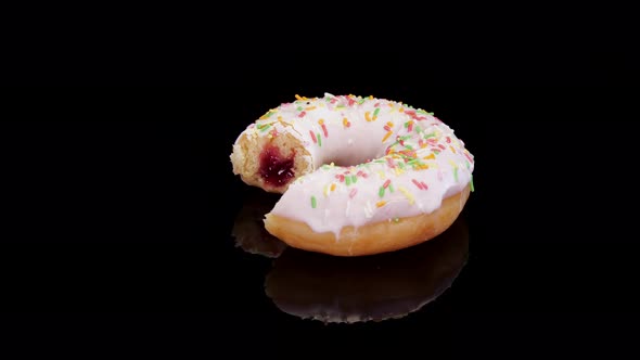 Donut with icing and colorful sprinkle rotating on a black background.