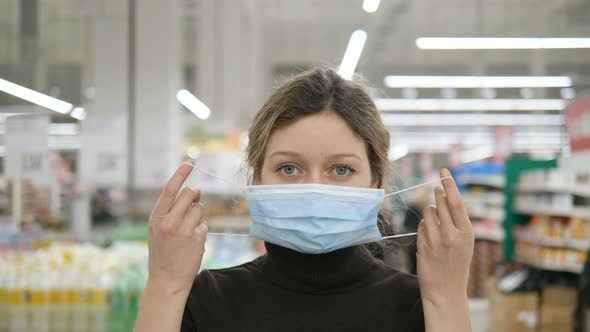 A Young Woman Puts on a Medical Mask in a Grocery Supermarket Close Up alt