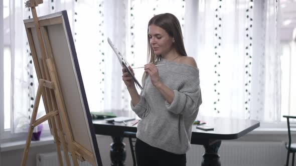 Confident Satisfied Woman Posing with Painting Palette Standing at Easel with Canvas Indoors alt