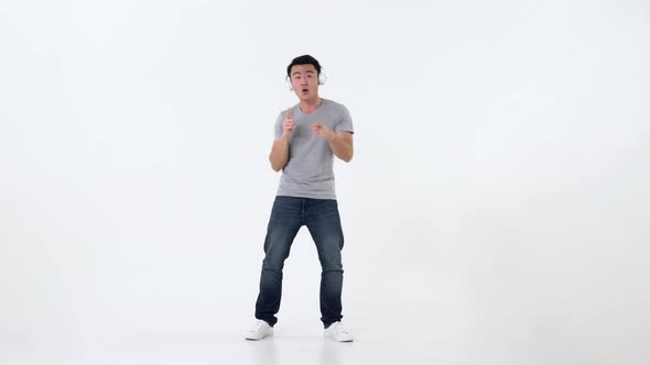 Cheerful handsome young asian man with headphones listening to music and dancing