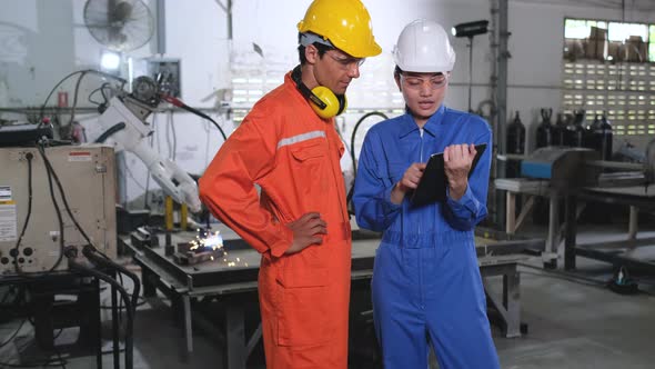 Two factory workers discuss about their work in front of welding robot machine working