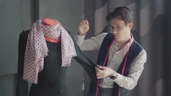 Focused Tailor Sewing Buttons of Elegant Black Dress Hanging on Mannequin in Atelier. Portrait  alt