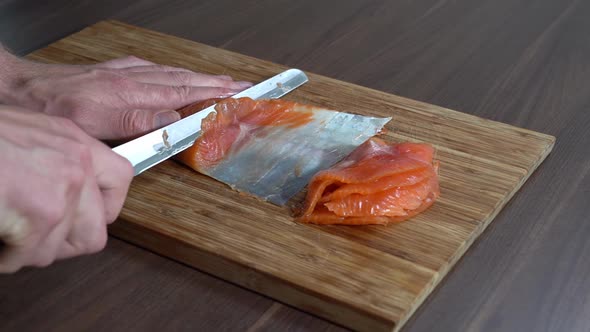 A male persons hand gently slicing smoked salmon on a wooden board with sharp knife - Static slow mo alt
