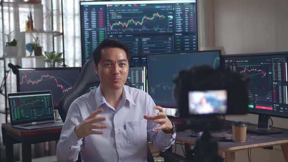 Asian Male Stock Market Broker Speech To Camera With Analyzing Graphs On Multiple Computer Screens alt