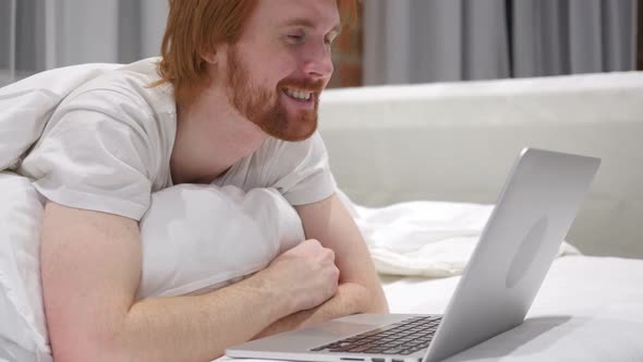 Online Video Chat By Excited Man Lying on Stomach in Bed alt
