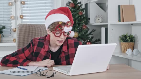 A Teenage Boy in Santa Hat and Funny Glasses Cheerfully Talks Via Video Communication Online on a