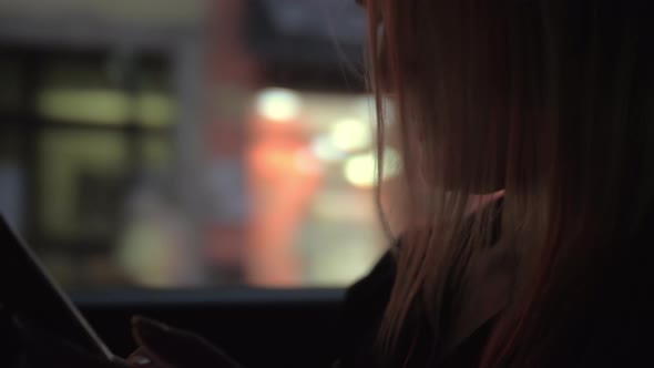 Woman with mobile in the car going in evening city alt