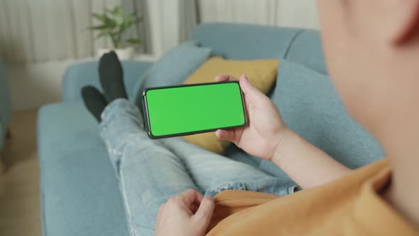 Male Using A Smartphone With Green Screen Mock Up Display At Home Living Room While Lying On Sofa alt