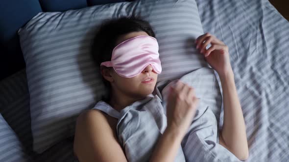 Woman in a Pink Eye Mask Lies Under a Blanket in a Bed and Suffers From Insomnia alt