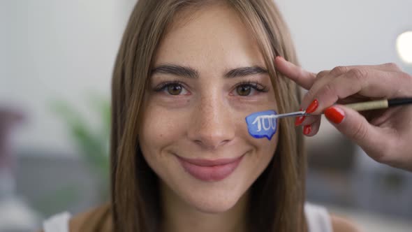 Close-up Portrait of Smiling Young Pleasant Woman Looking at Camera While Artist Painting Message alt