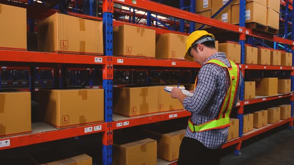 Asian man stocking up with barcodes on a box placed on a steel shelf in a warehouse.