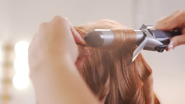 Female Hairdresser Curling Hair to Redhead Girl in Beauty Salon Slow Motion alt