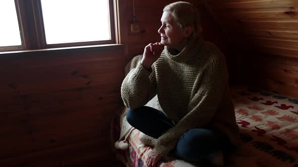 Woman in Old Age Sits By the Window and Looks Alone Into the Distance