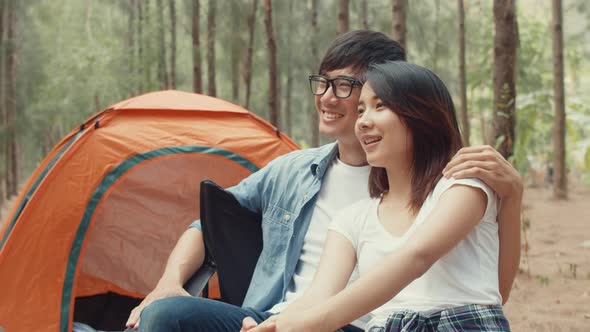 Young asia campers couple sitting in chairs by tent in forest.