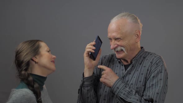 Woman Stands and Looks at Senior Man Holding Black Telephone alt