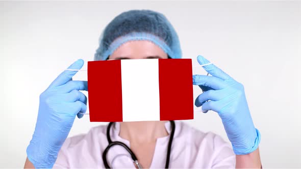Close-up. Doctor in Glasses, Blue Medical Cap, Gloves Holds in Hands Medical Mask with Peru Flag alt
