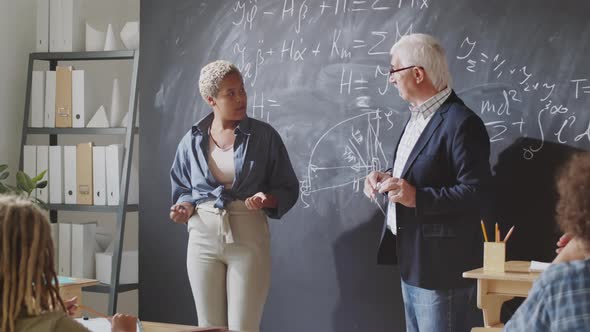 Female High School Student Talking with Professor by Chalkboard alt