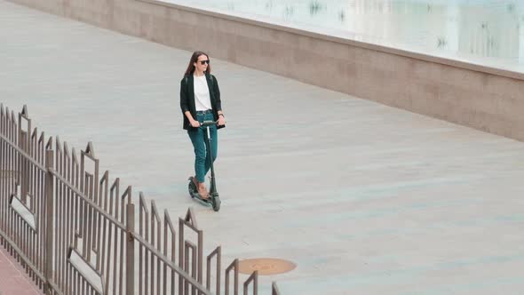 Woman Walking On Electric Scooter Down Embankment alt
